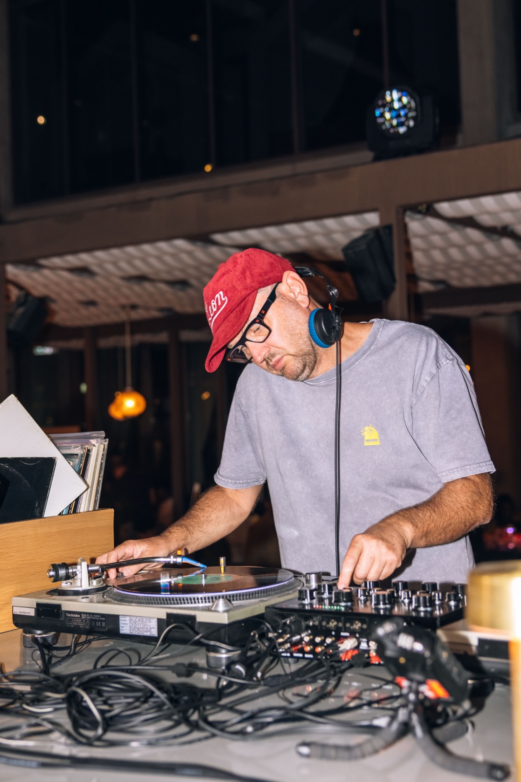 A DJ in a red cap and glasses mixing at the decks.