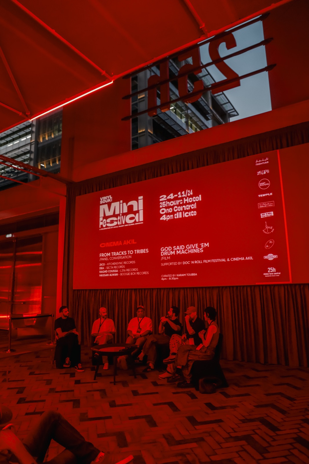 People seated in front of the Mini Festival programme projected on a red-lit wall.