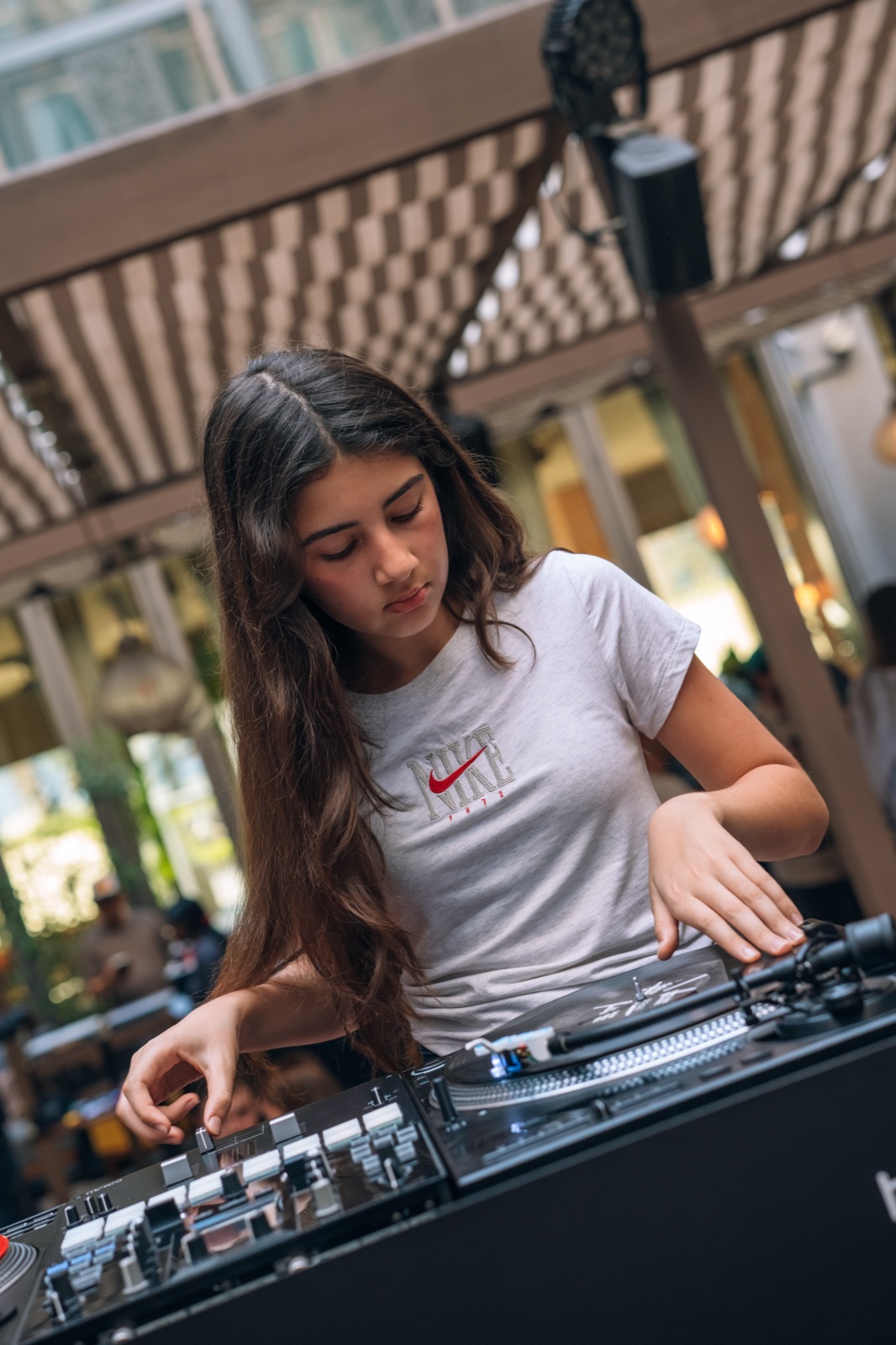 A young DJ in a white T-shirt concentrating at the decks under a striped awning.