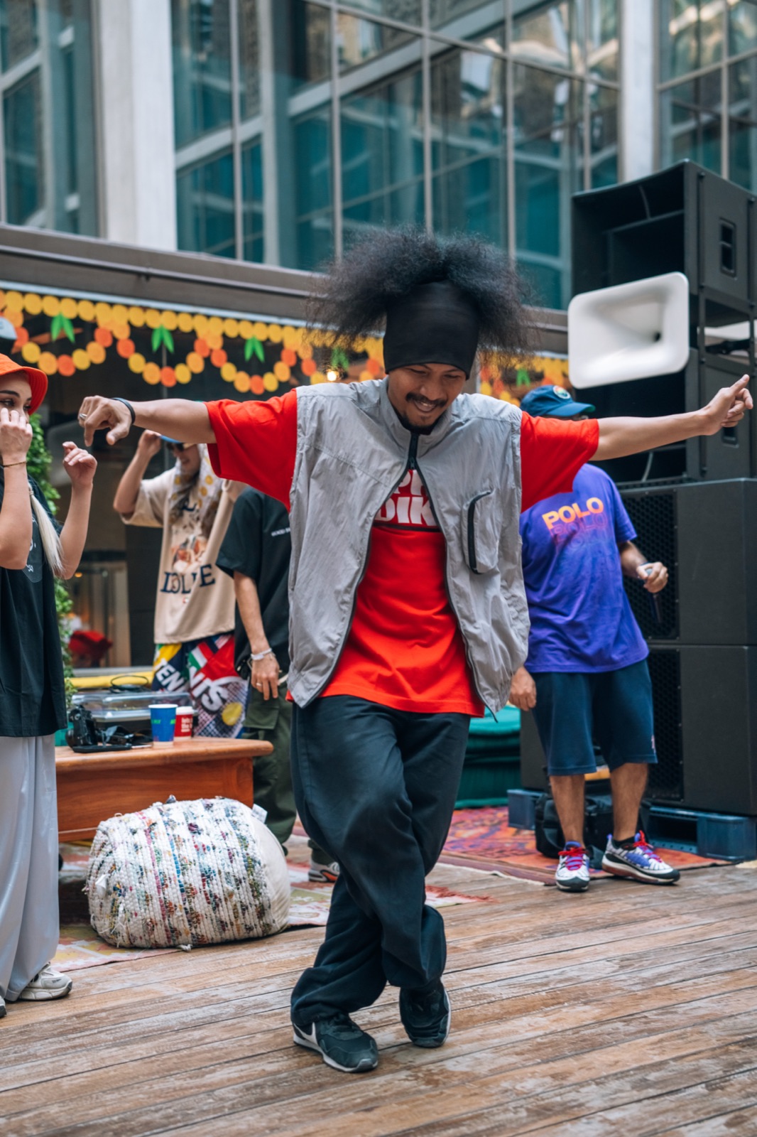 A dancer in a grey vest and red T-shirt posing with arms out.