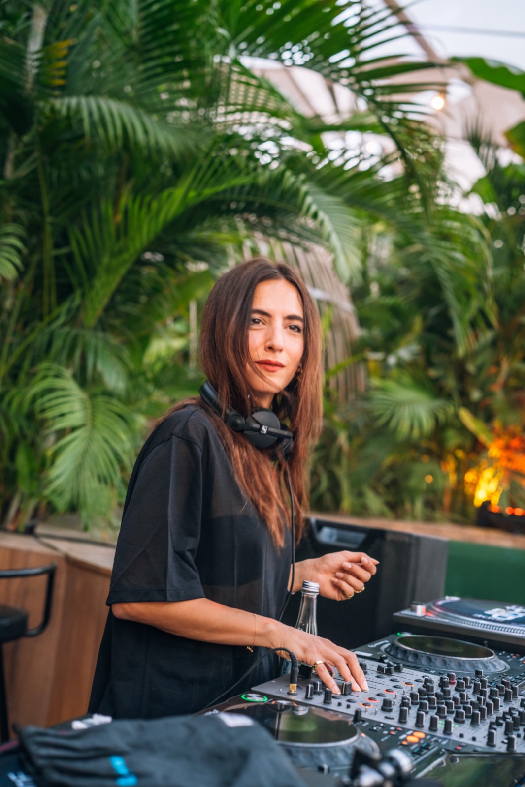 A DJ smiling at the decks among palm leaves.