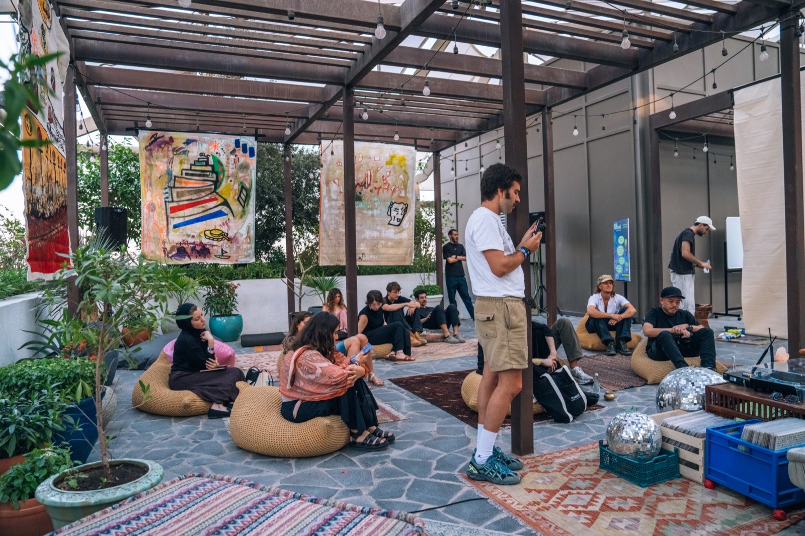 People relaxing on bean bags in a shaded courtyard with hanging artworks.