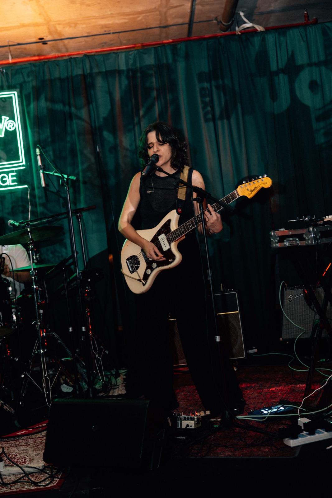 A guitarist playing on stage in front of a green curtain.