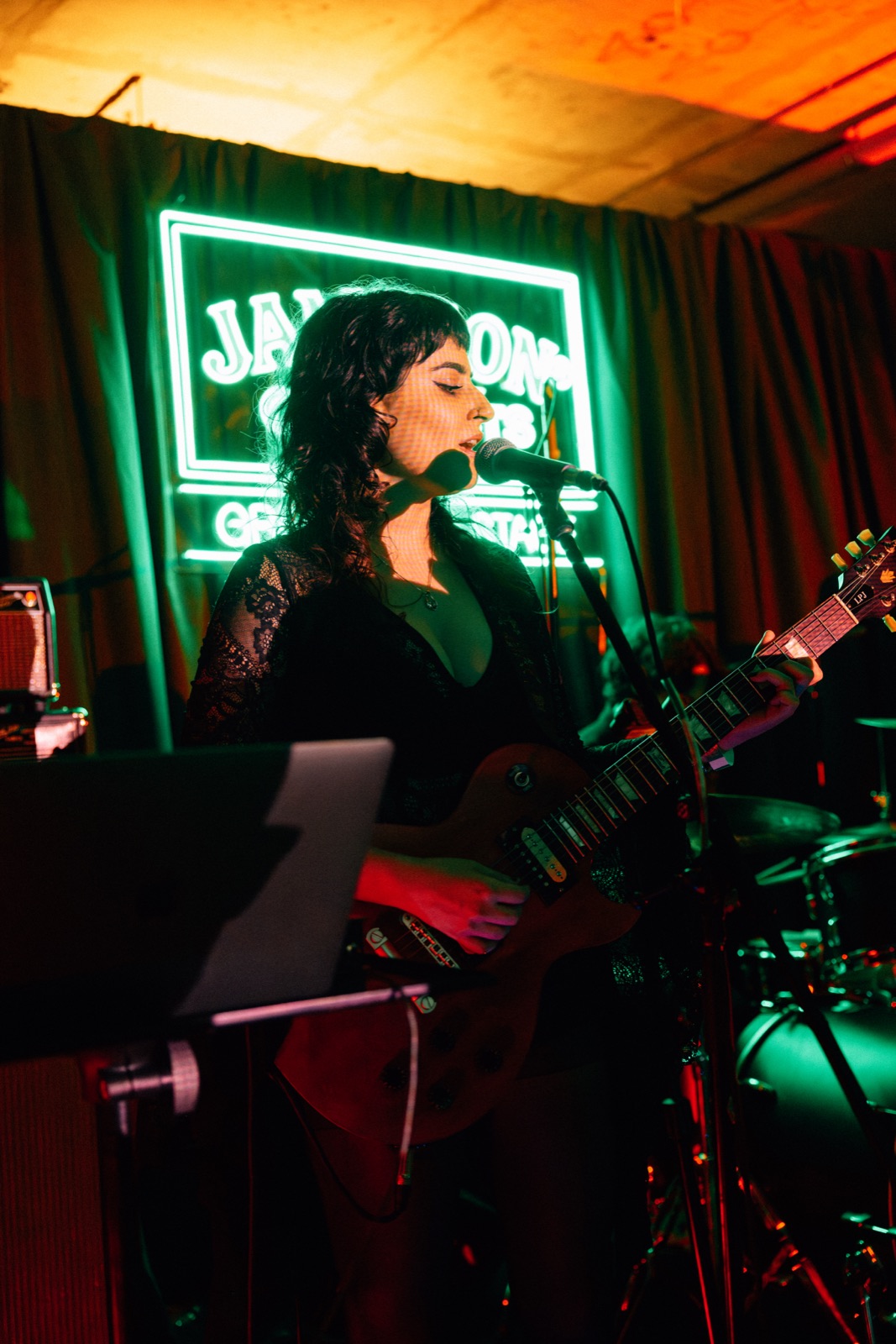 A singer at a keyboard on stage, under a green neon sign.