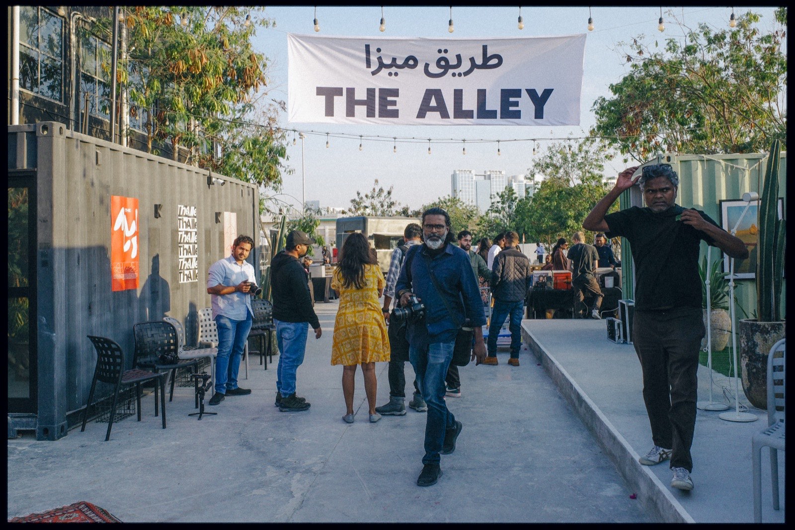 People walking under a banner reading The Alley in English and Arabic.