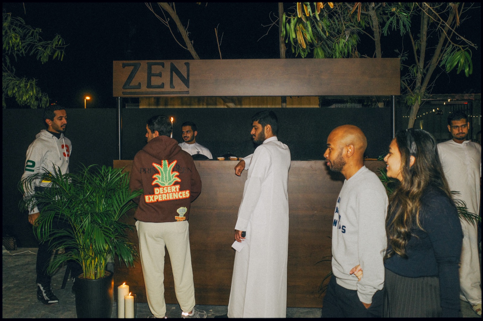 People talking at a bar with a Zen sign at night.