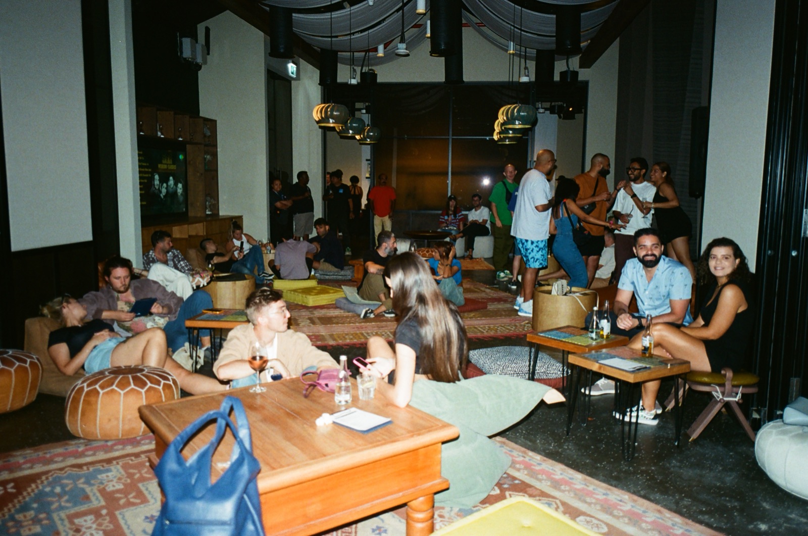 A lounge full of people at tables and sofas during a record fair, with rugs on the floor.
