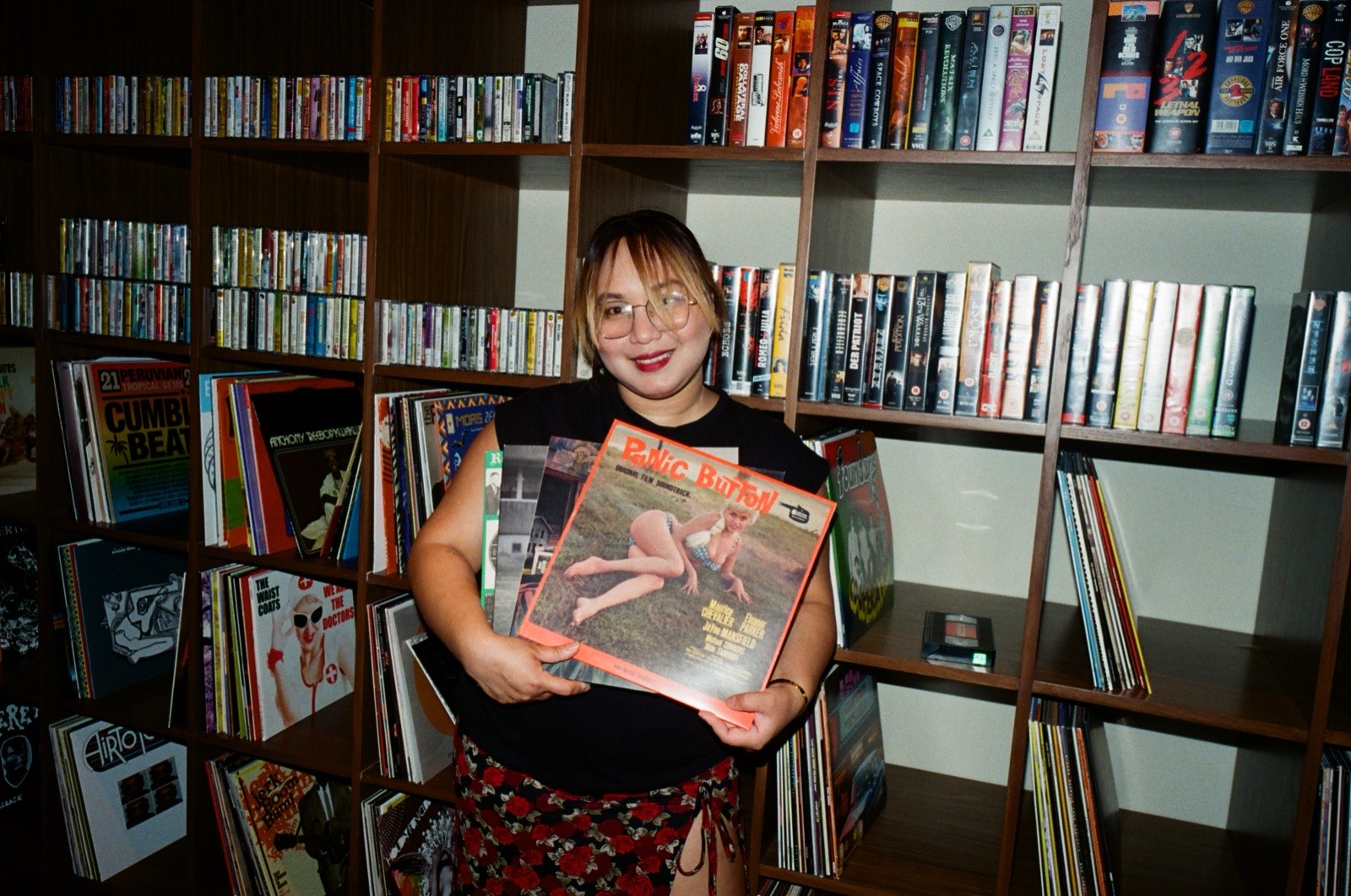 A woman holding up a record in front of bookshelves.