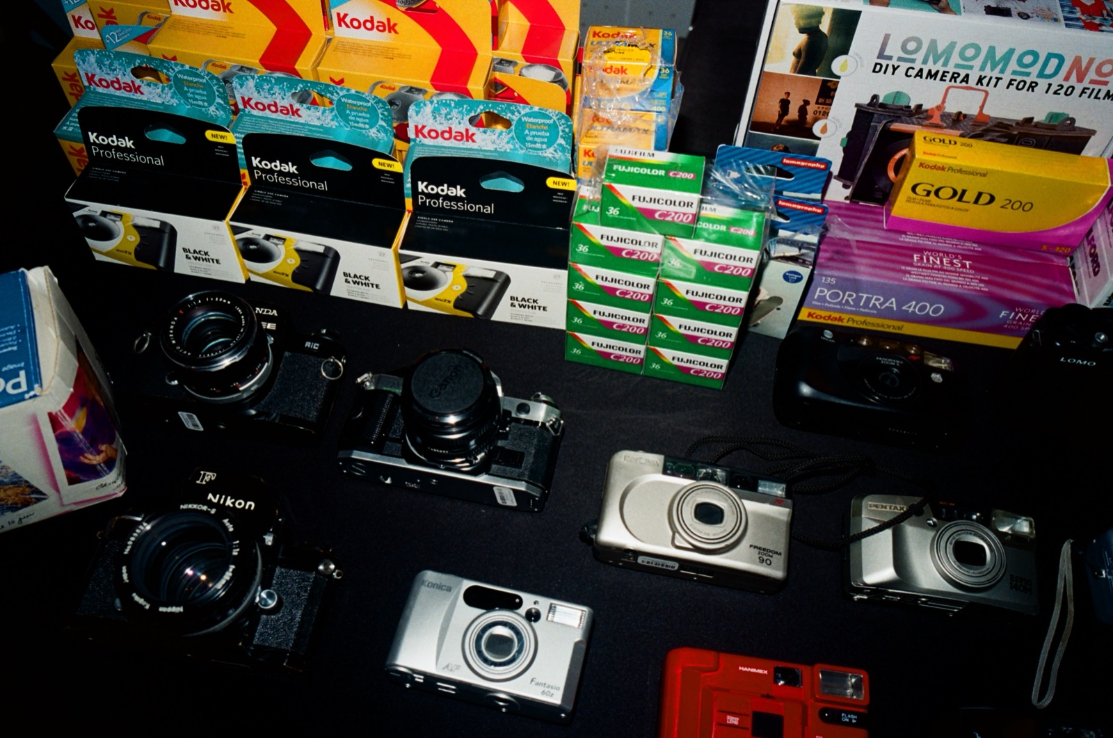 A table of film cameras and boxes of camera film for sale.