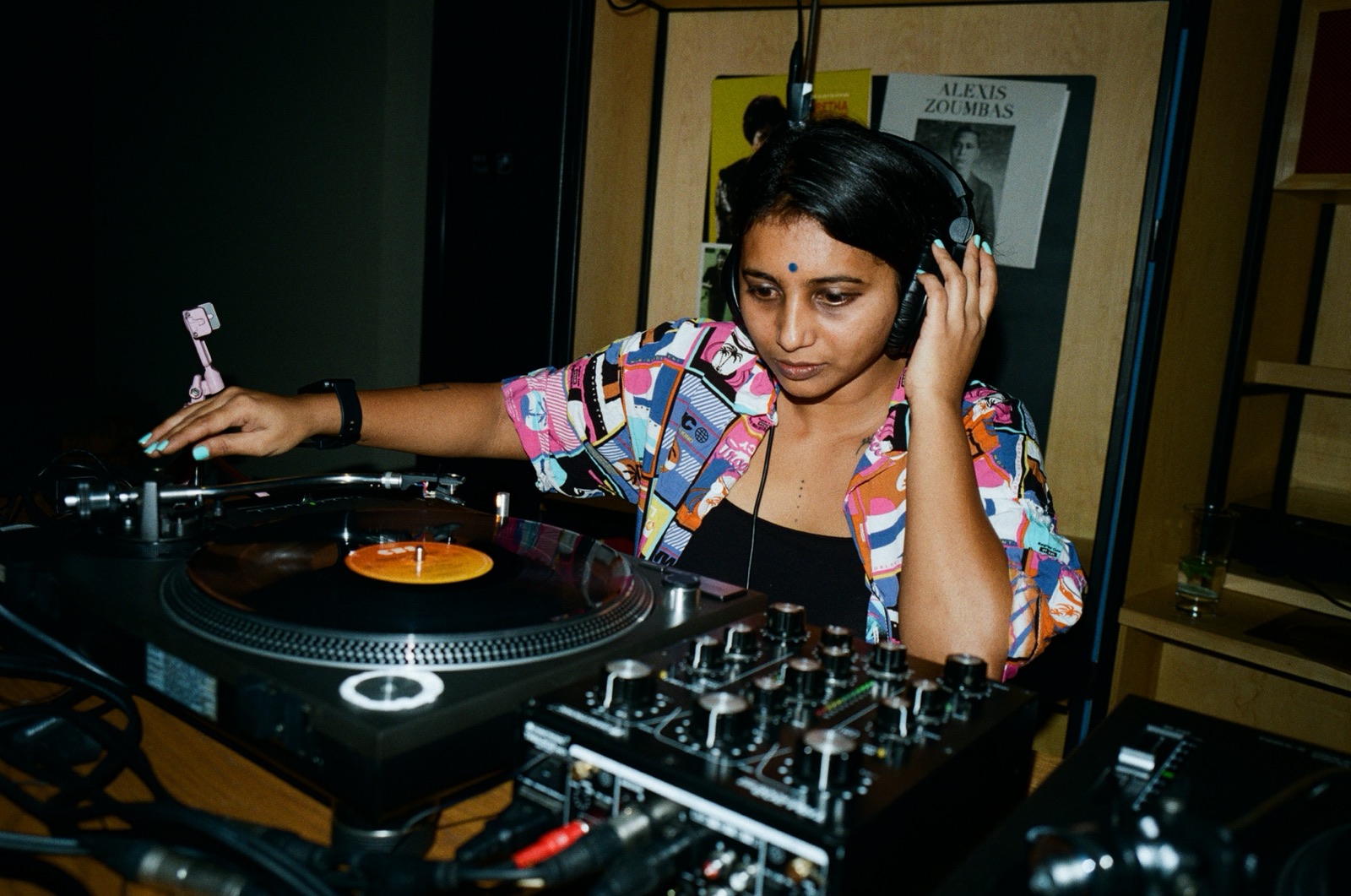 A DJ in headphones and a patterned shirt playing a record.