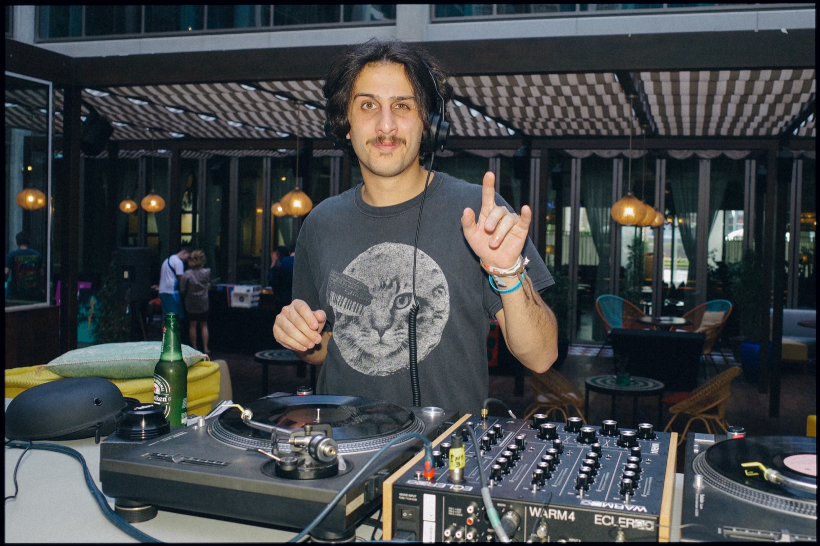 A DJ smiling and pointing up at the decks on a terrace.