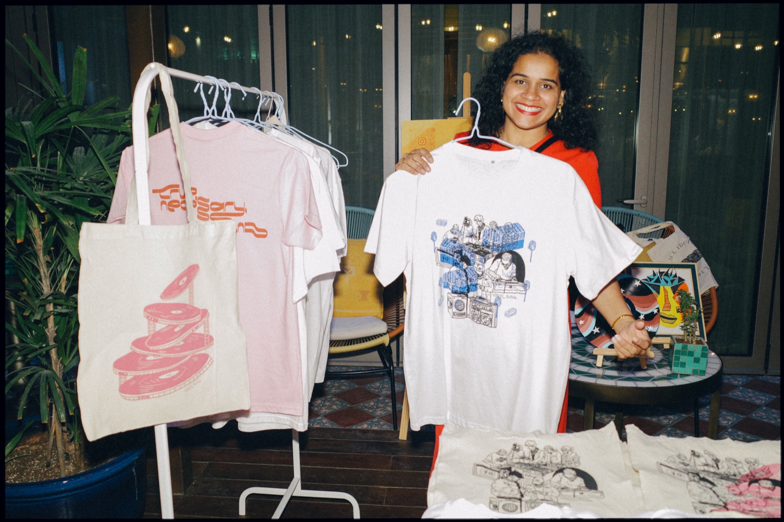 A woman holding up a printed T-shirt at a clothing stall.