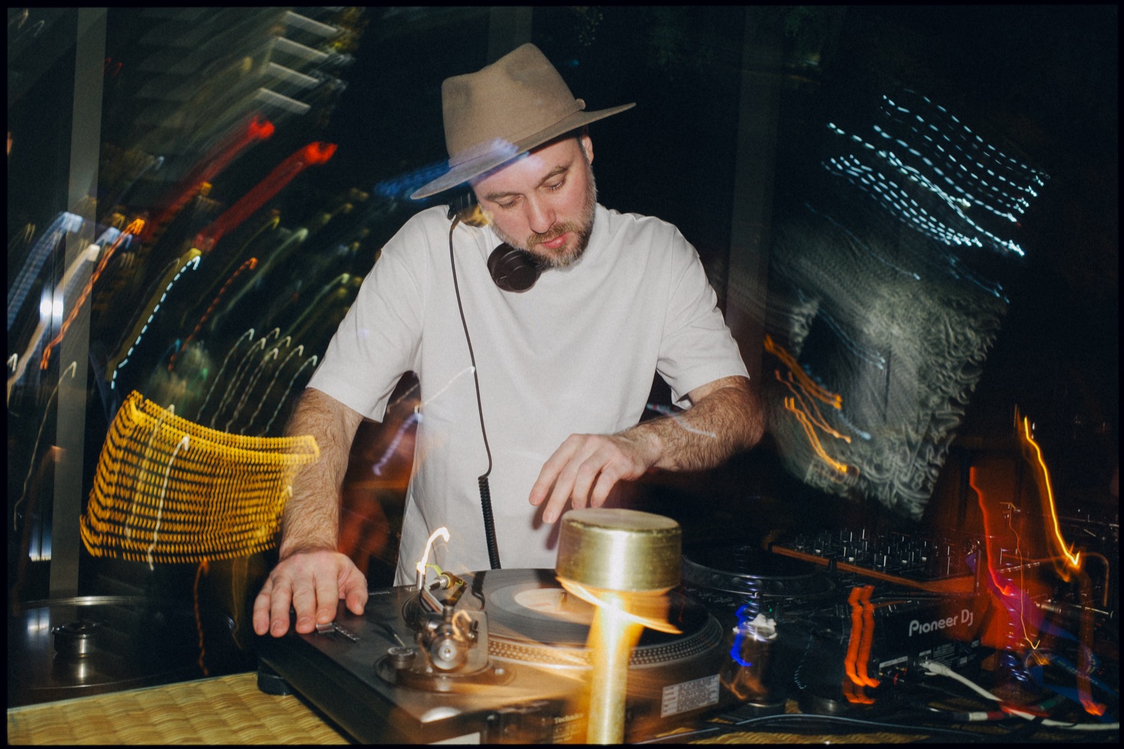 A DJ in a hat at the decks, with light trails.