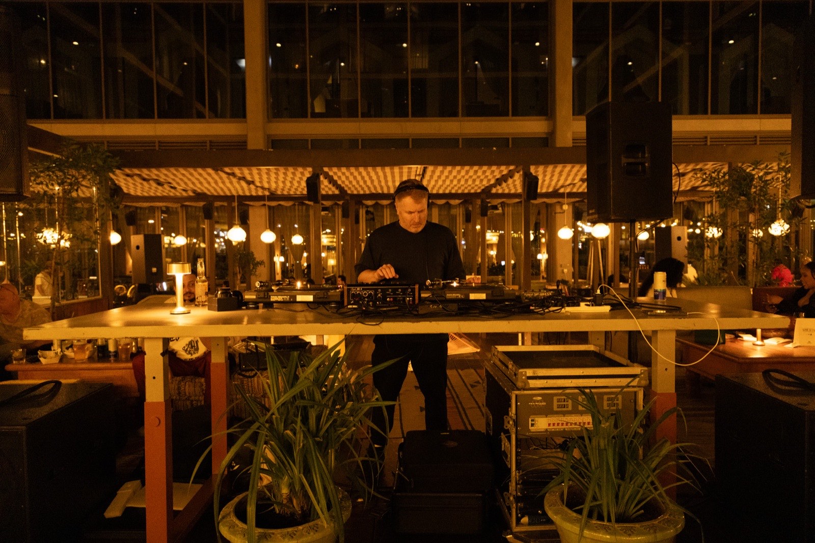 A DJ at a long booth on the terrace at night.