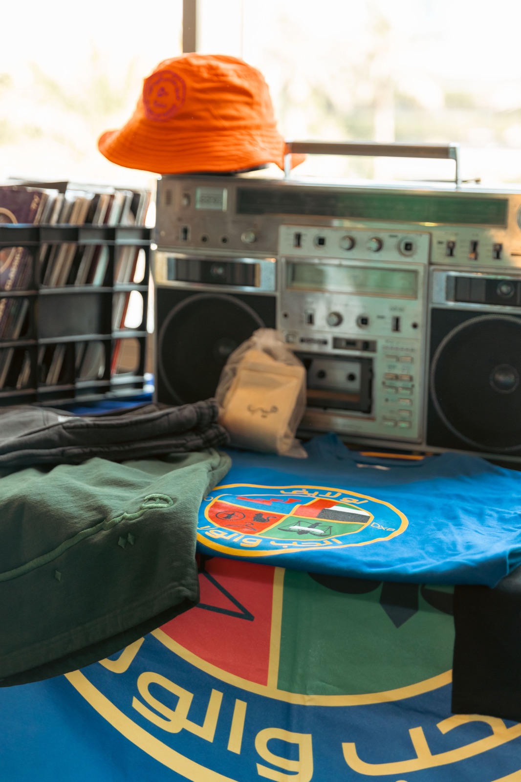 A vintage boombox and speakers on a table, with a bucket hat and a flag.