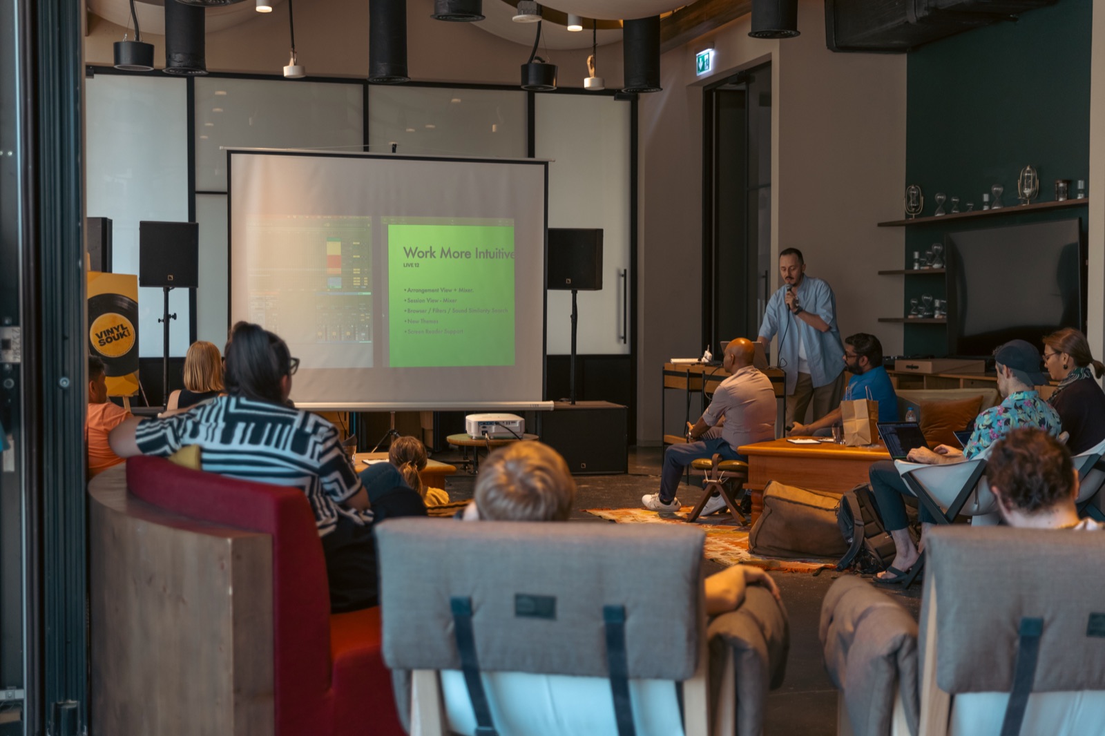 People seated watching a talk, with slides on a screen.