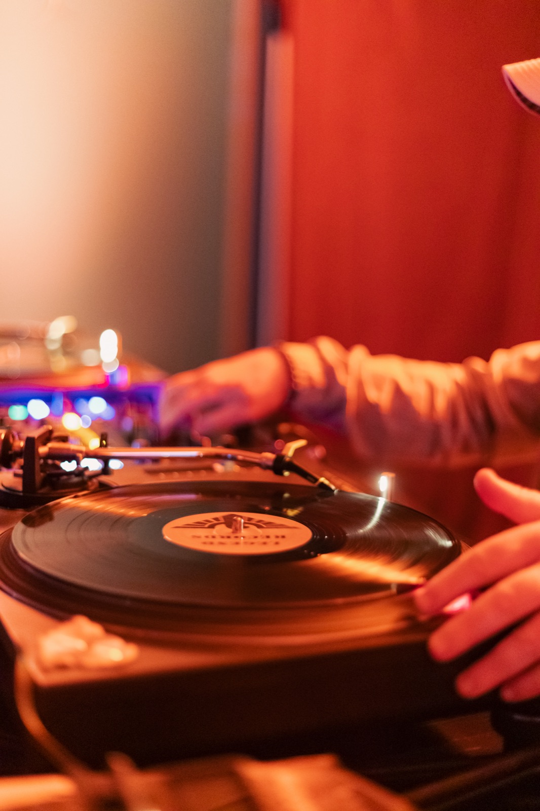 Hands placing a record on a turntable in red light.