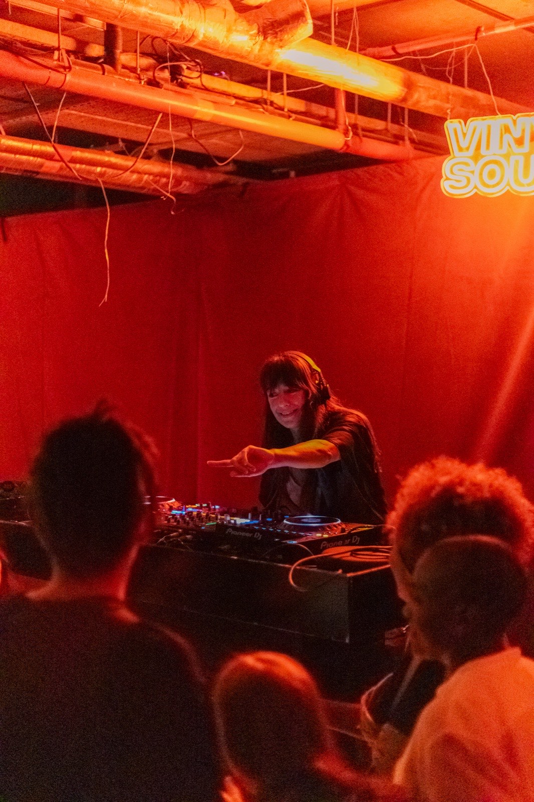 A DJ playing to a crowd in a red-lit room, under a Vinyl Souk neon sign.
