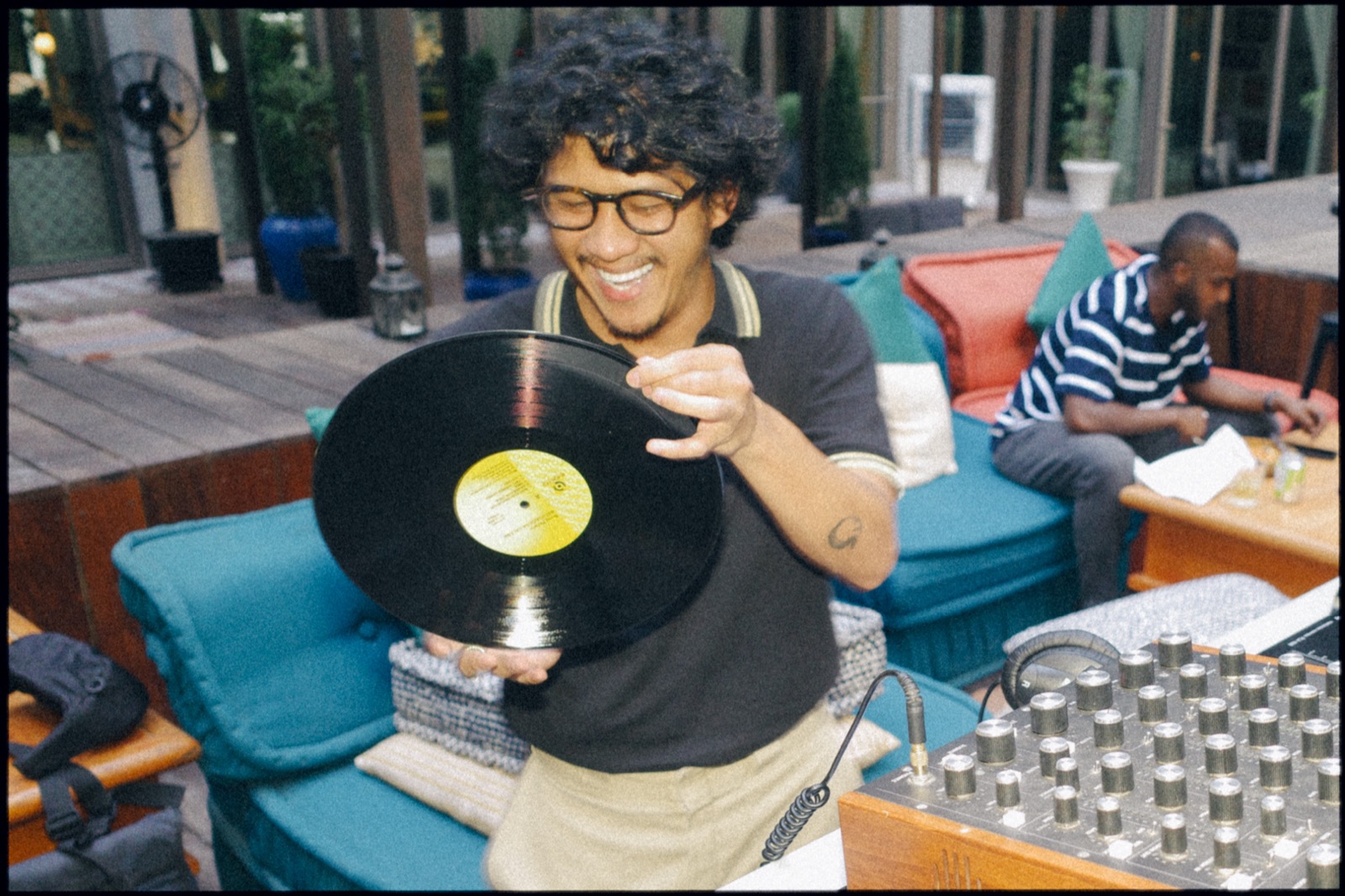 A man laughing as he holds up a vinyl record on a terrace.