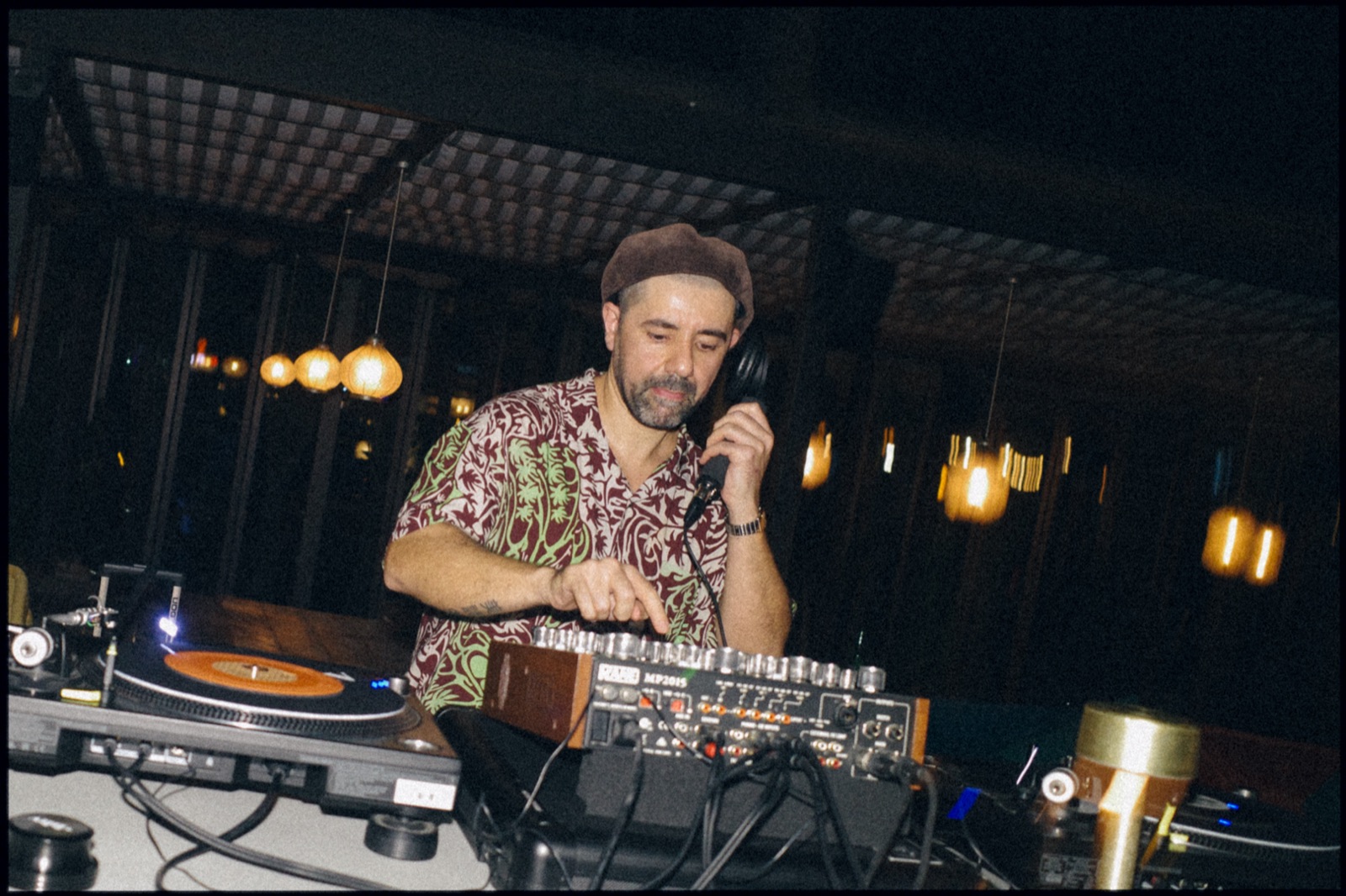 A DJ in a patterned shirt at a rotary mixer on an evening terrace.