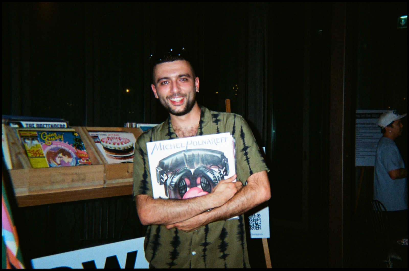 A man smiling as he holds a record to his chest beside a record stall.