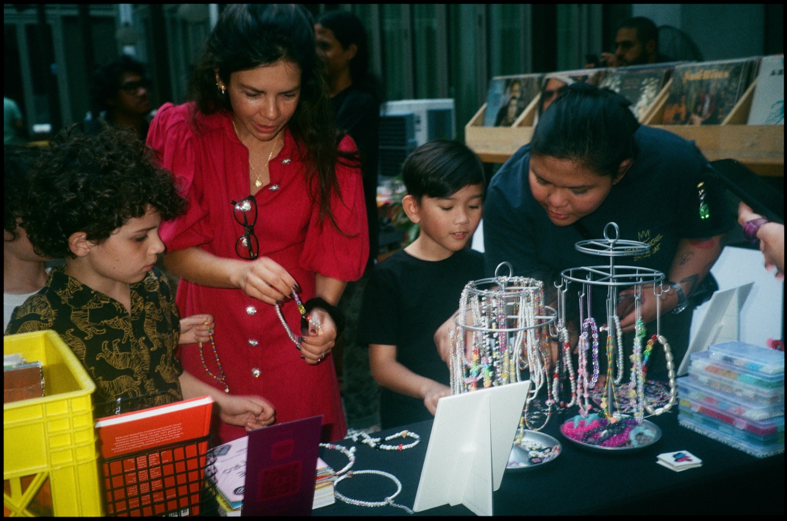 Children and adults looking at a jewellery stall beside a yellow crate of records.