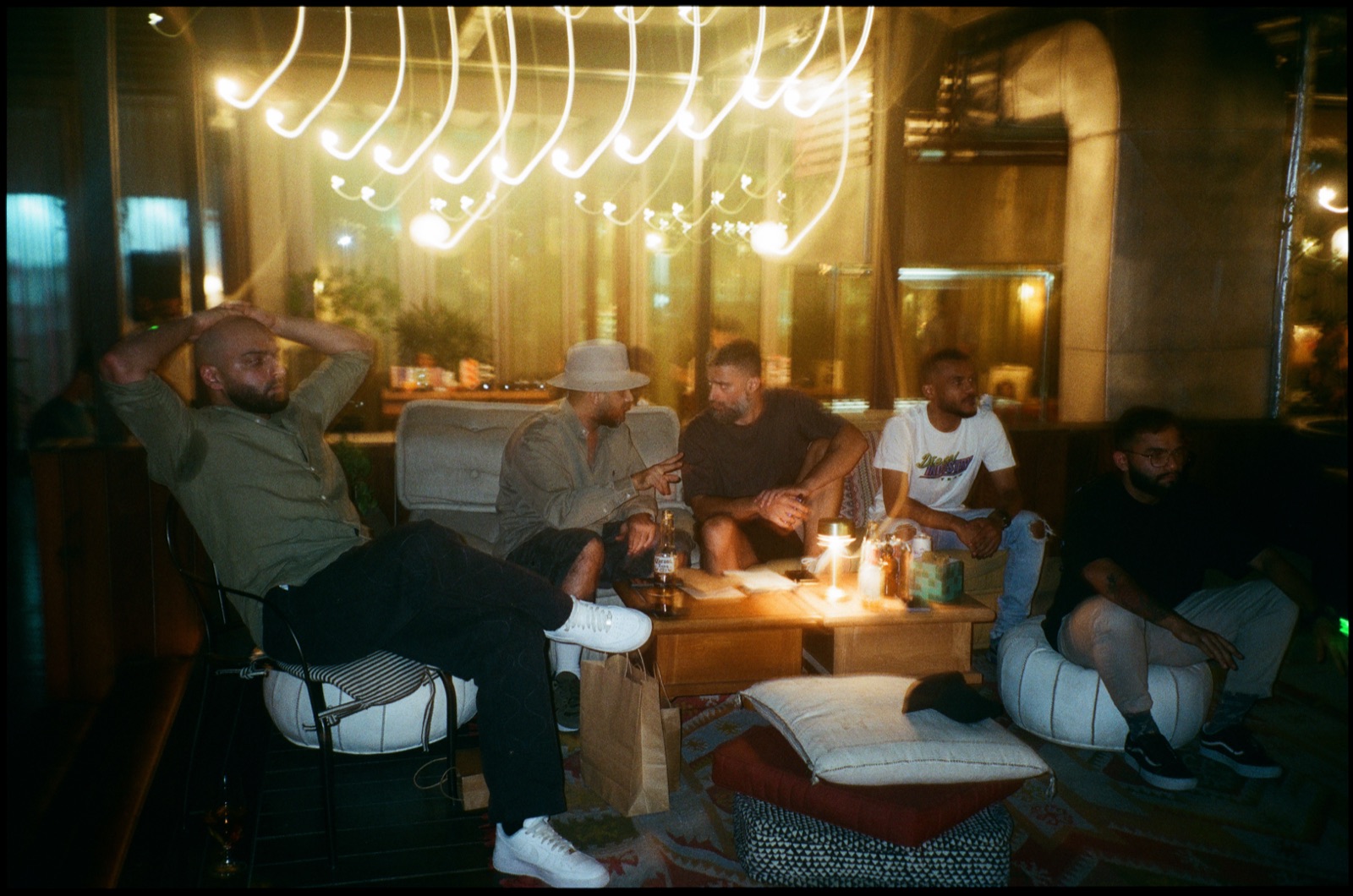 People relaxing on floor cushions under strings of lights at night.