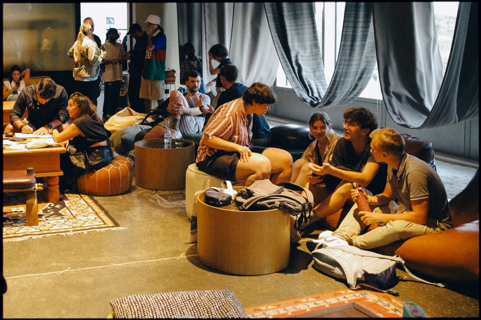 People lounging on cushions and low tables in a room with sheer curtains.