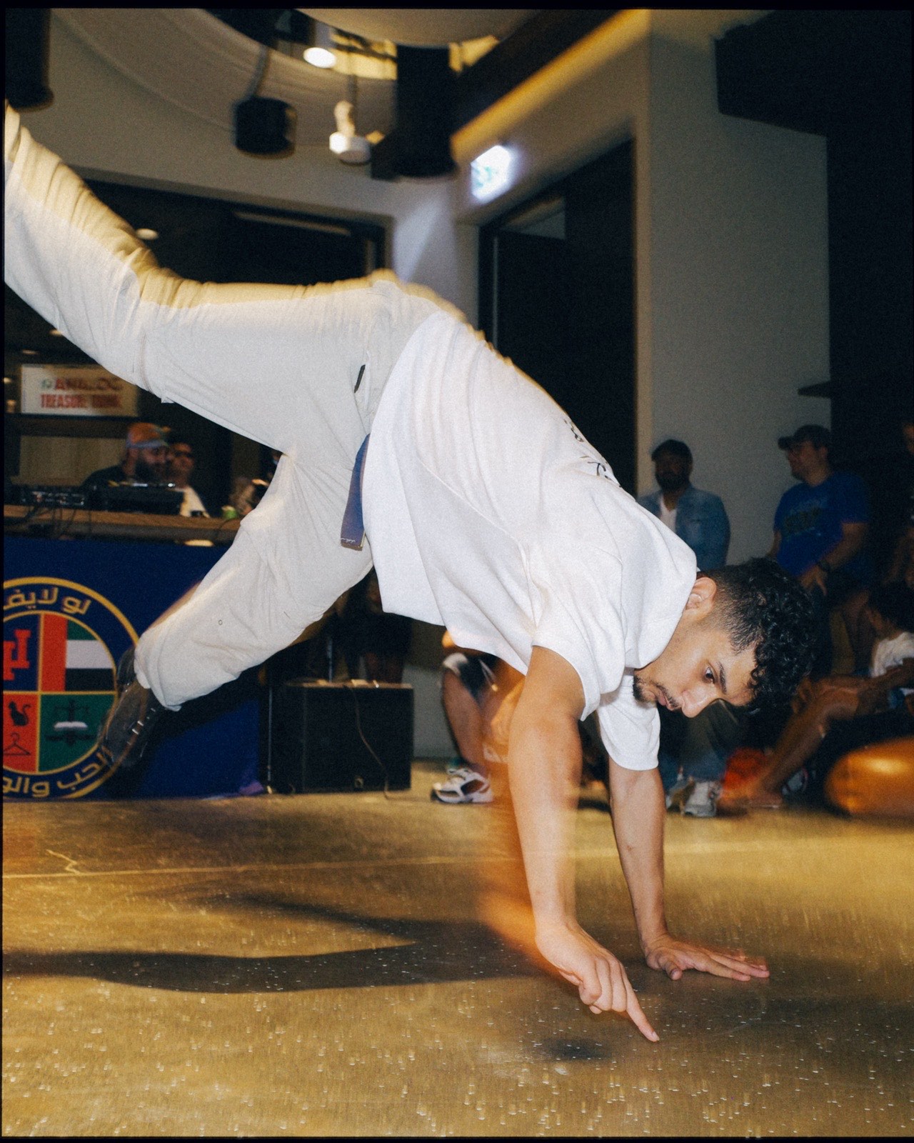 A breakdancer in a white T-shirt doing a handstand freeze.
