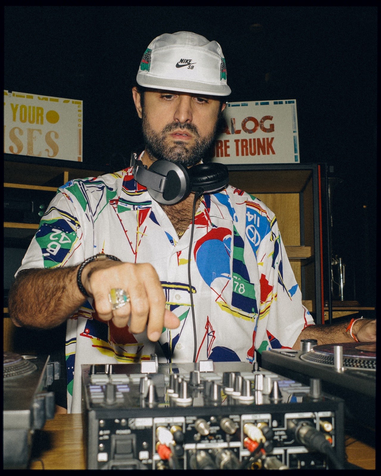 A DJ in a white cap and patterned shirt at the mixer.