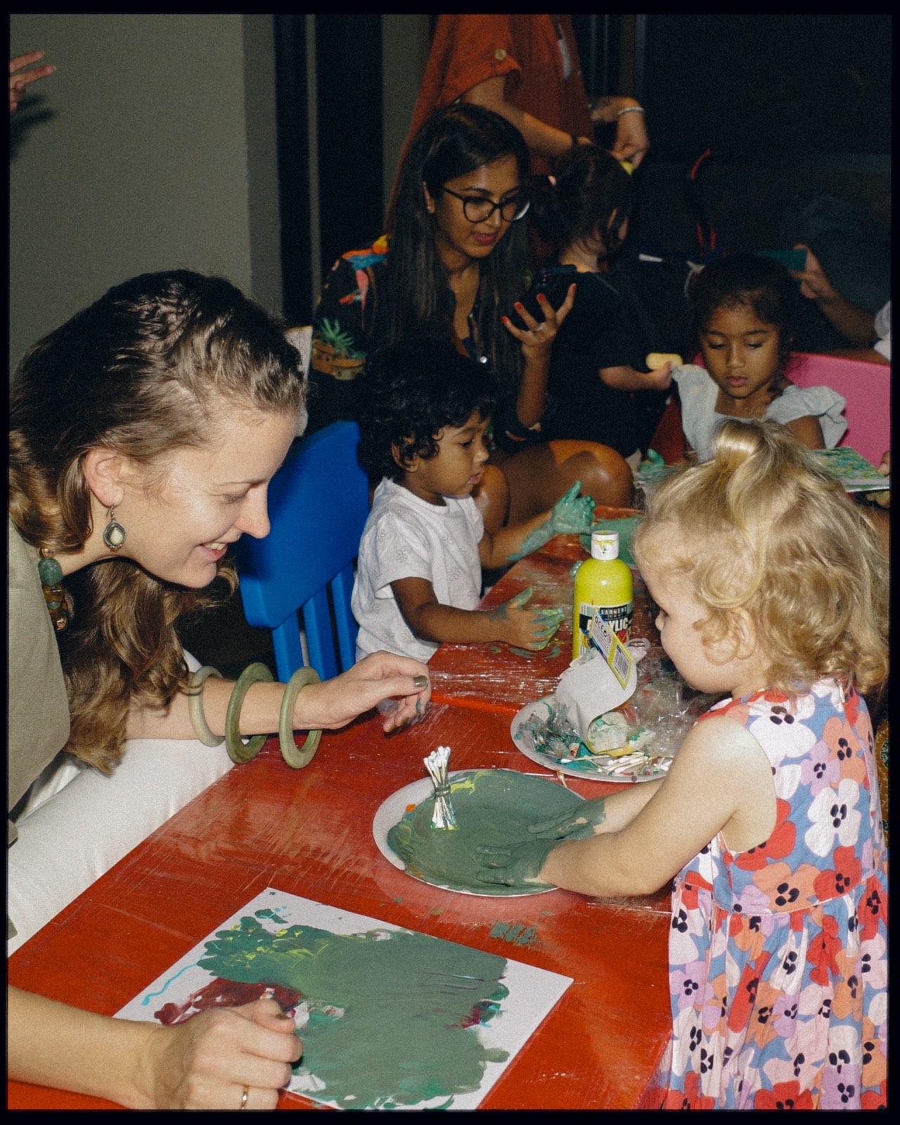 A small child painting at a table with other children and adults.