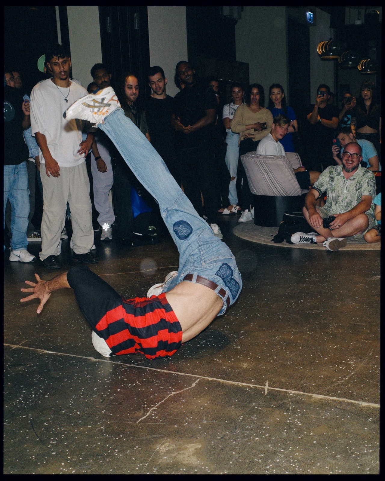 A breakdancer balancing on one hand with legs in the air, watched by a crowd.