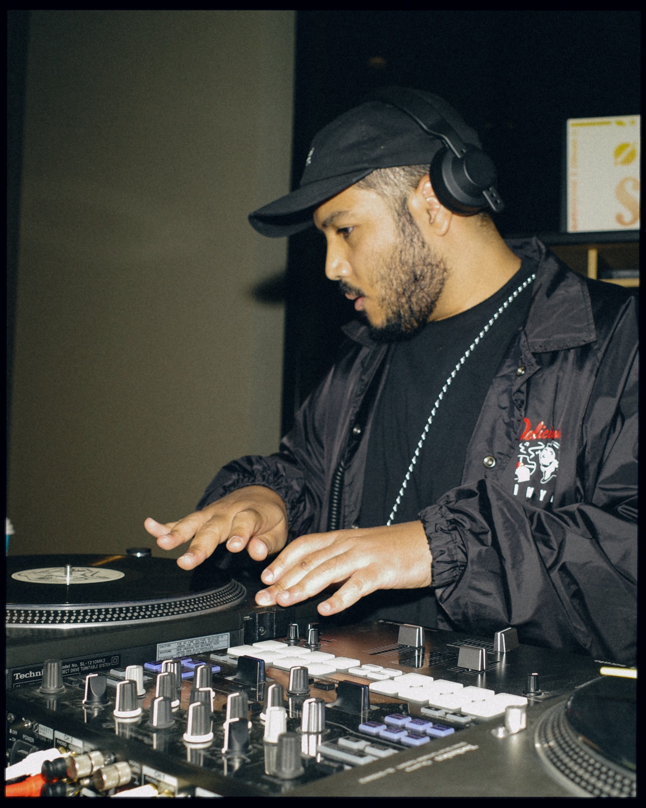 A DJ in a black cap and headphones with both hands on the decks.