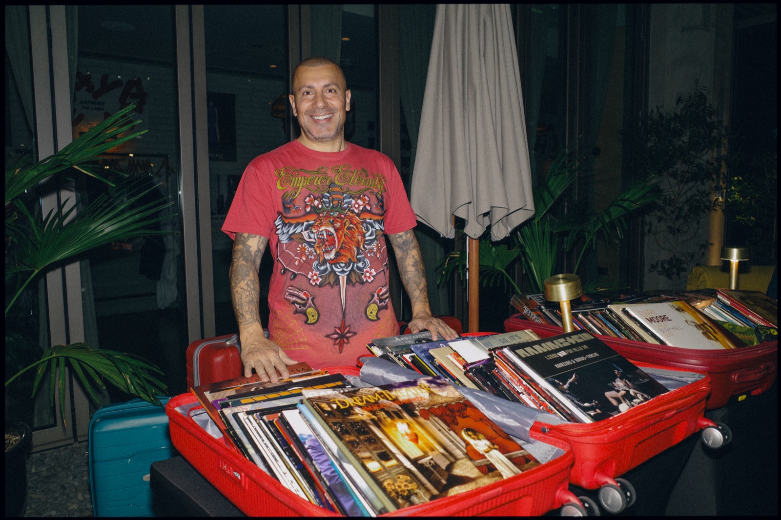 A man in a red T-shirt behind open red cases of records.
