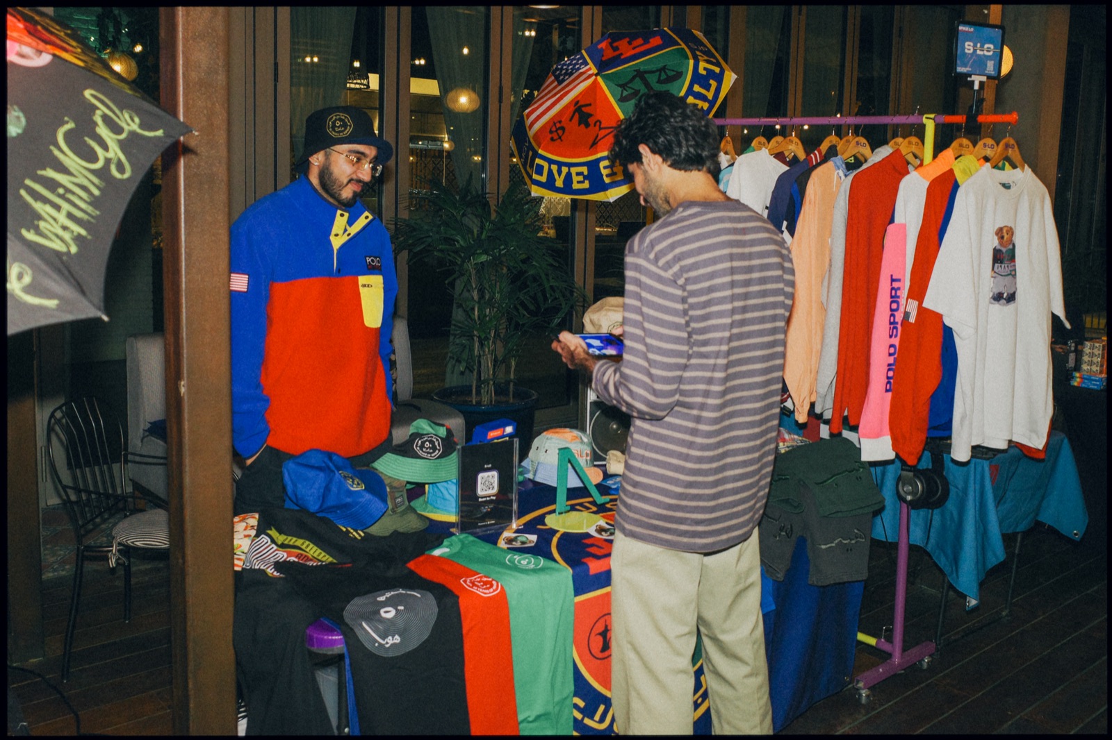 A clothing rail of colourful jackets and T-shirts, with people browsing.