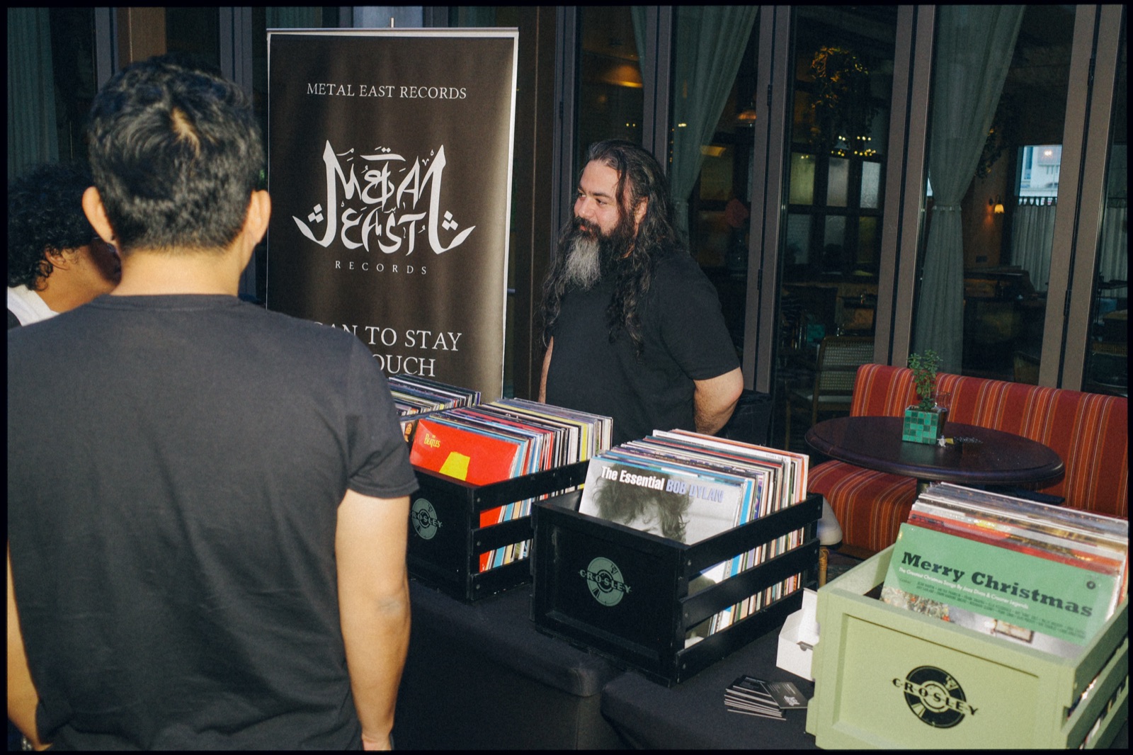 Two people talking at a record stall with crates of vinyl.