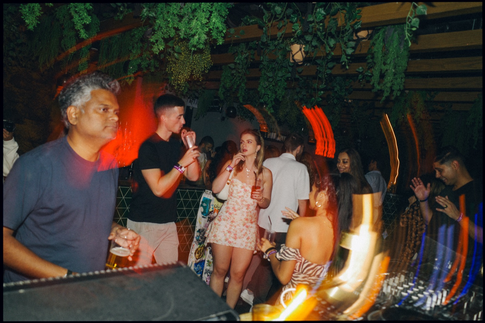 People dancing near the DJ booth at night, with light trails.