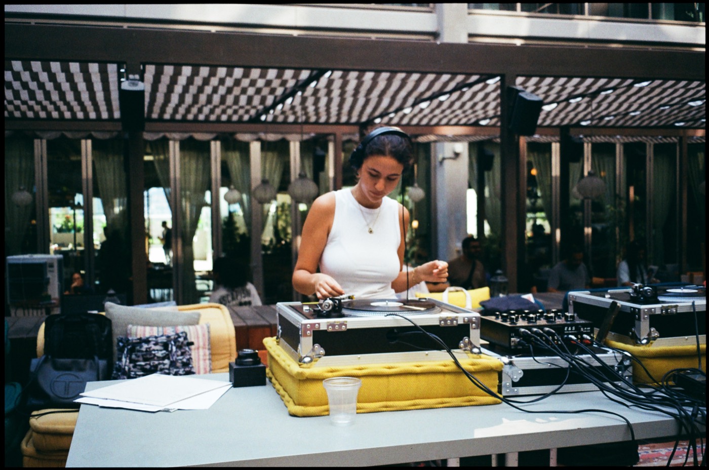 A DJ in headphones cueing a record at an outdoor set under a striped canopy.